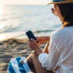 Woman using smartphone with AI travel assistant while relaxing by the sea in Lefkada