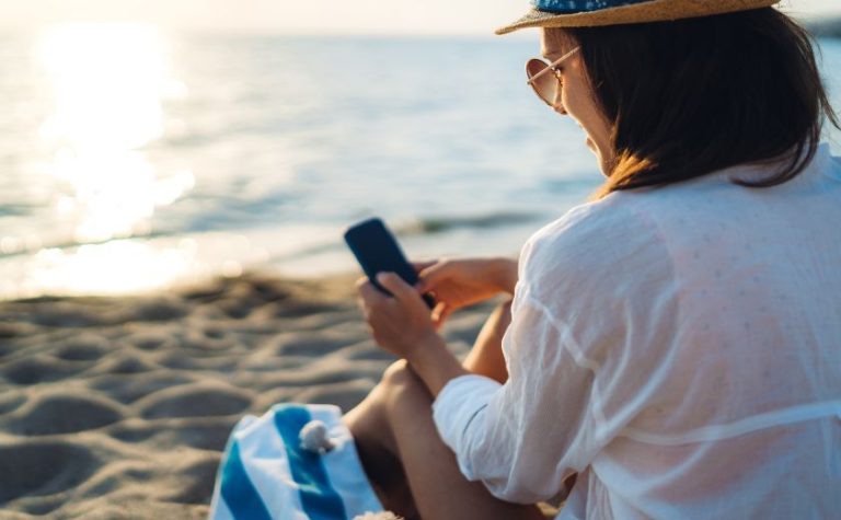 Woman using smartphone with AI travel assistant while relaxing by the sea in Lefkada